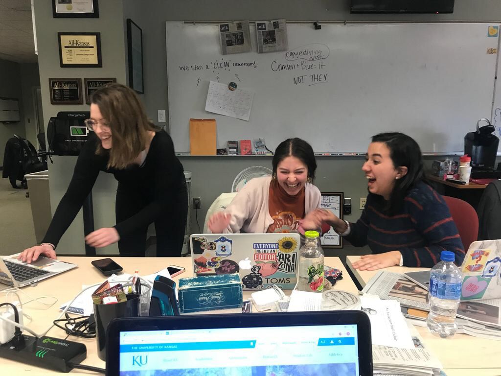 Savanna Smith, Nichola McDowell and Nicole Asbury laugh while sitting at a table in the newsroom of the UDK